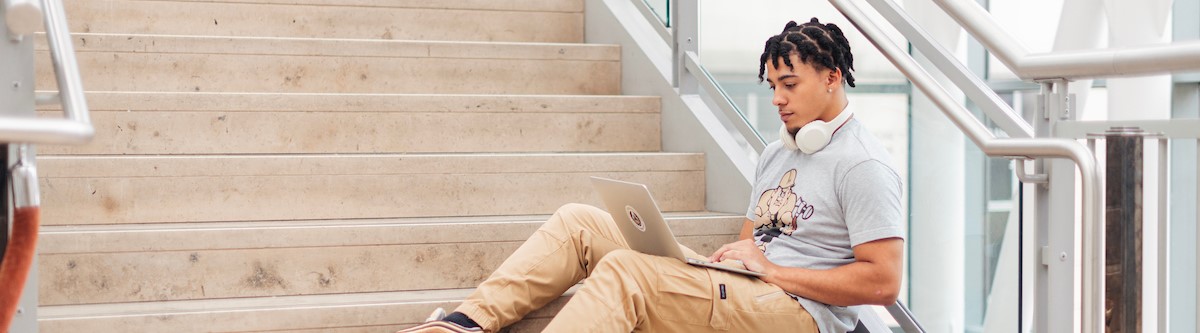 pictured: student sitting on a staircase working on his laptop