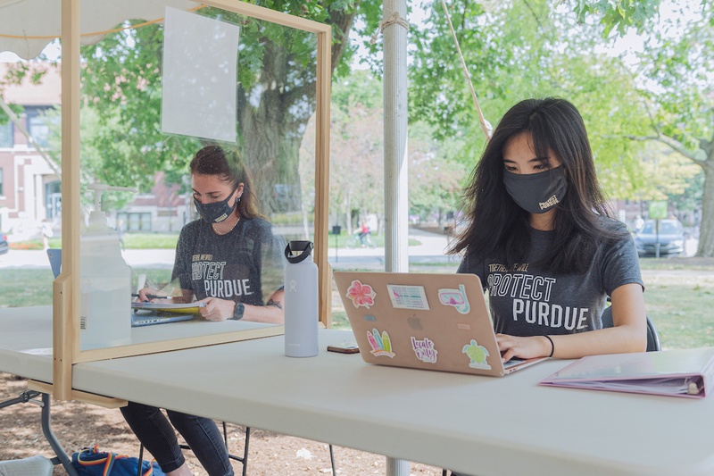 Two Purdue students working on laptops outside