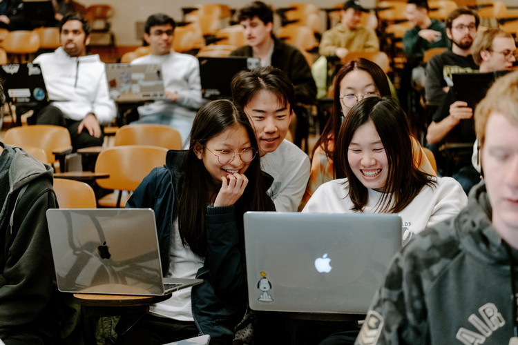 Smiling students in a theater-style classroom looking at their laptops.