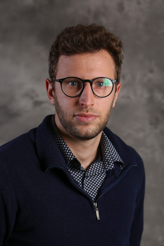 Student wearing a grey shirt and glasses, with a dark grey background.