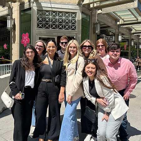 A group of students pose outside of a building, smiling.