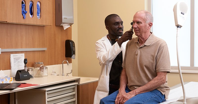 A male nurse uses an otoscope to look in an older man's ear.