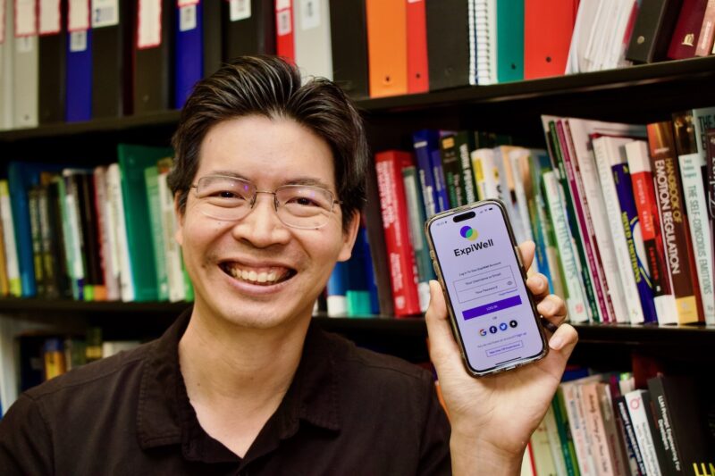 Louis Tay holds his cell phone displaying the ExpiWell app welcome screen.