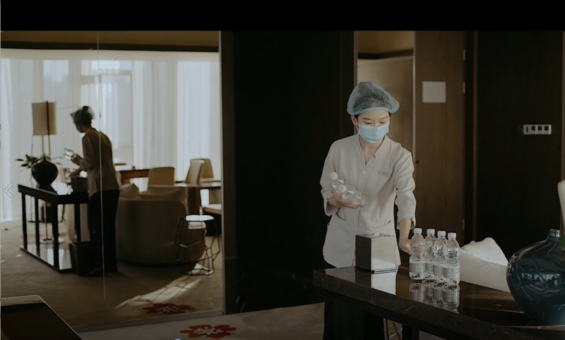 A hotel worker places water bottles on a desk.