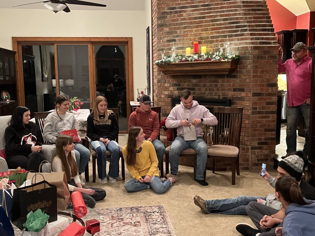 Several members of the Purdue Hort Club sitting on chairs and couches with one of them opening their white elephant gift.