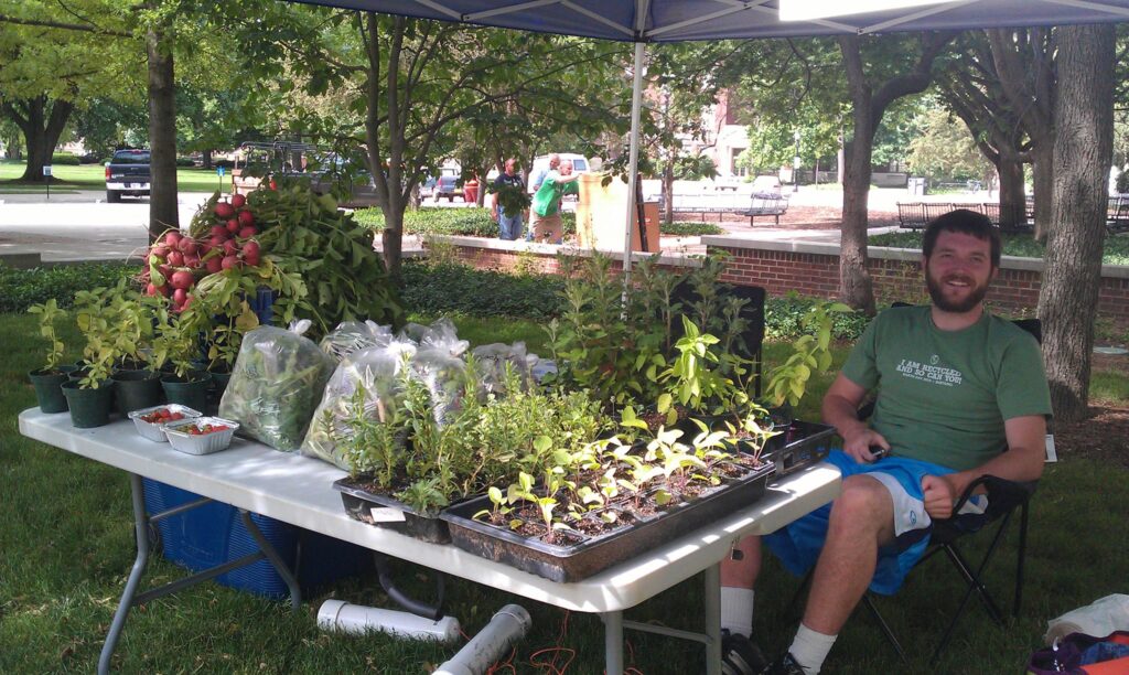 Chris sitting at an outdoor table of produce and plants.