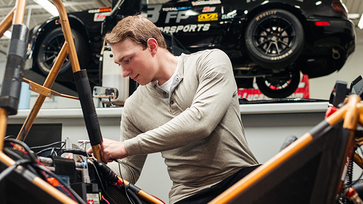 A male college student in a motorsports lab working on a car.