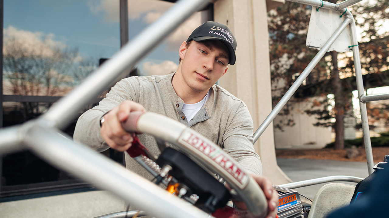 Male college student wearing a Purdue University in Indianapolis cap attaching a steering wheel to a go kart.