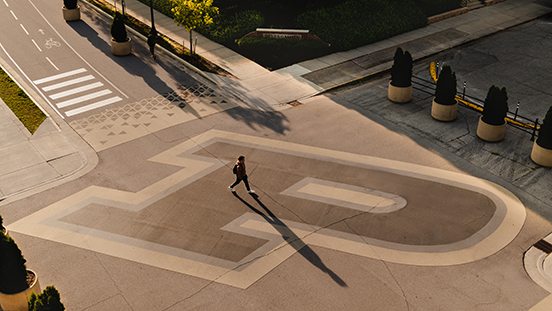 A Purdue student walking across an intersection featuring a large Motion P mark.  