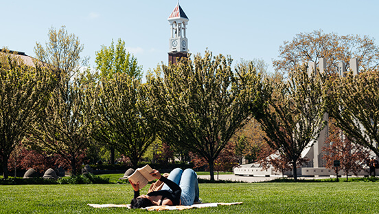 A Purdue student reads a book outdoors on campus.   