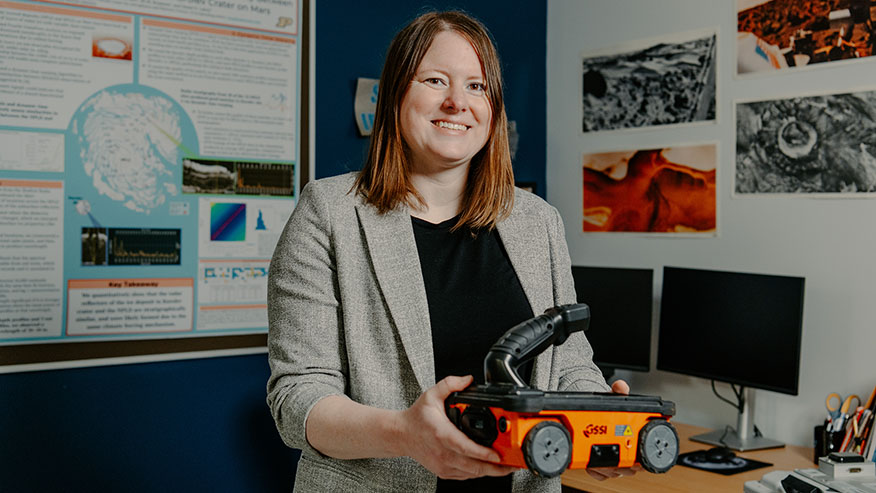 A Purdue professor stands in her office, holding a land-based mobile radar system