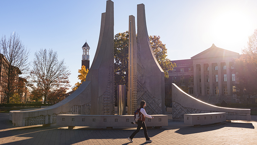 A student walks in front of a fountain on Purdue University’s campus.