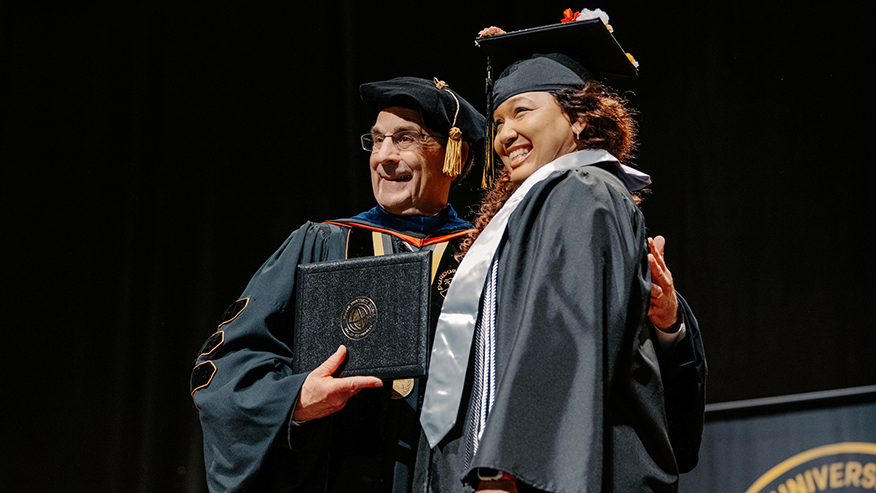 A student and chancellor smile and pose at a Purdue Global commencement ceremony.