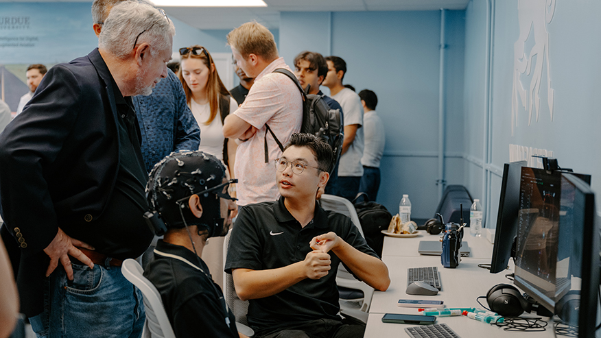 Two students (seated) talk with engineer (standing) during a flight simulation exercise.