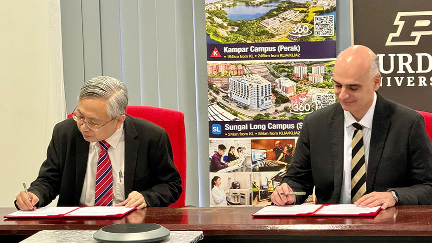 Two men in suits seated at a table sign agreements in front of them.