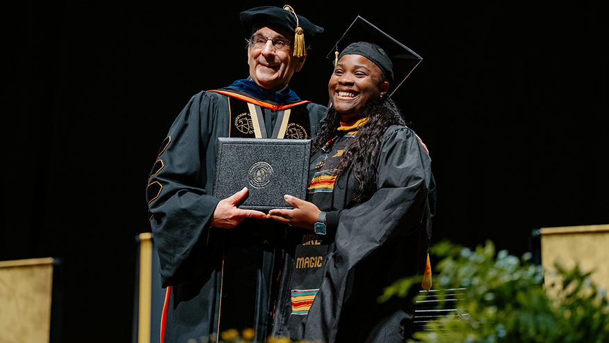 Purdue Global Chancellor Frank Dooley awards a diploma to a graduate.