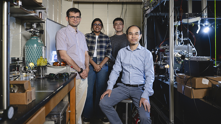 Three Purdue University researchers stand and one sits in a dark laboratory, looking directly at the camera.