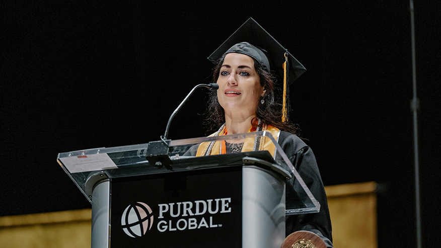 Emily Lewis standing behind a lectern at Purdue Global’s October commencement