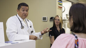 A doctor and medical assistant visit with someone near a patient room.