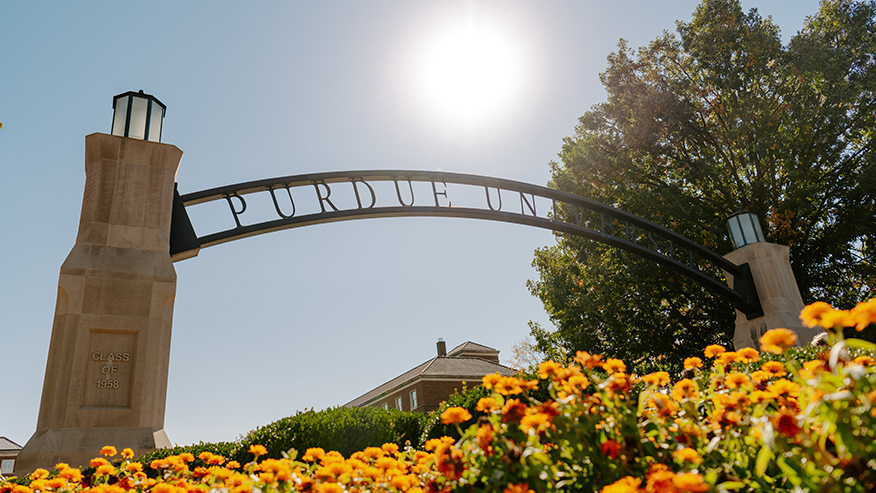 Purdue University’s Gateway to the Future Arch from below with fall flowers in the foreground.