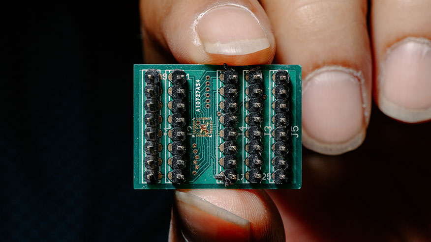 A close-up of an integrated circuit chip held between an index finger and thumb.