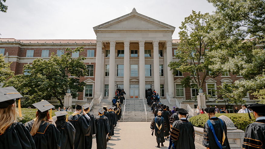 Students wearing graduation regalia enter Elliot Hall of Music for a commencement ceremony