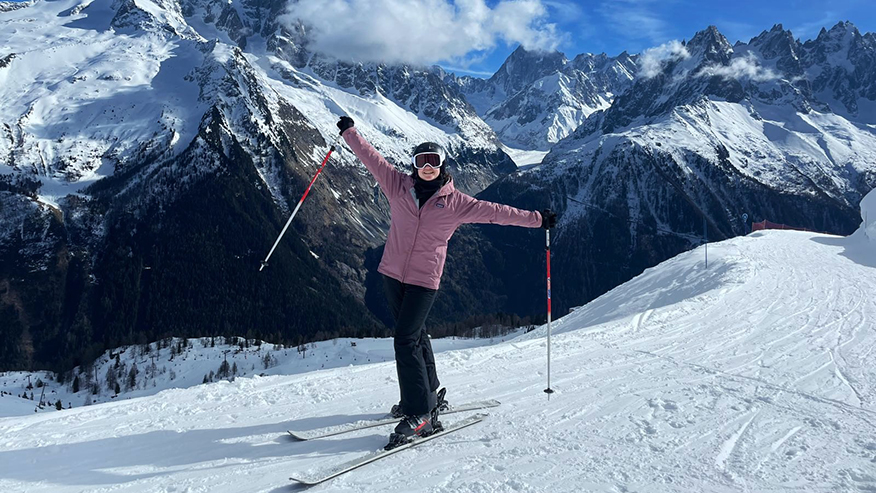 A person wearing ski gear stands in snow atop a mountain.