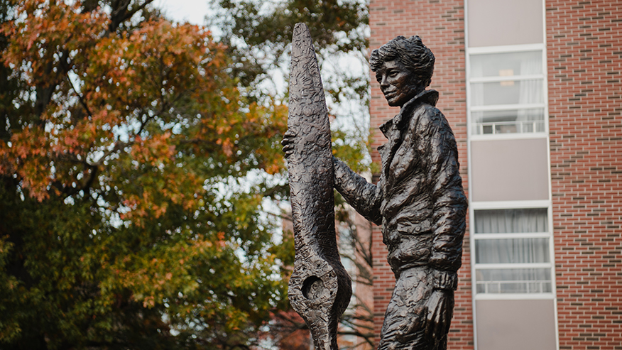 The bronze Amelia Earhart statue on Purdue University’s campus with Earhart Hall and fall trees in the background