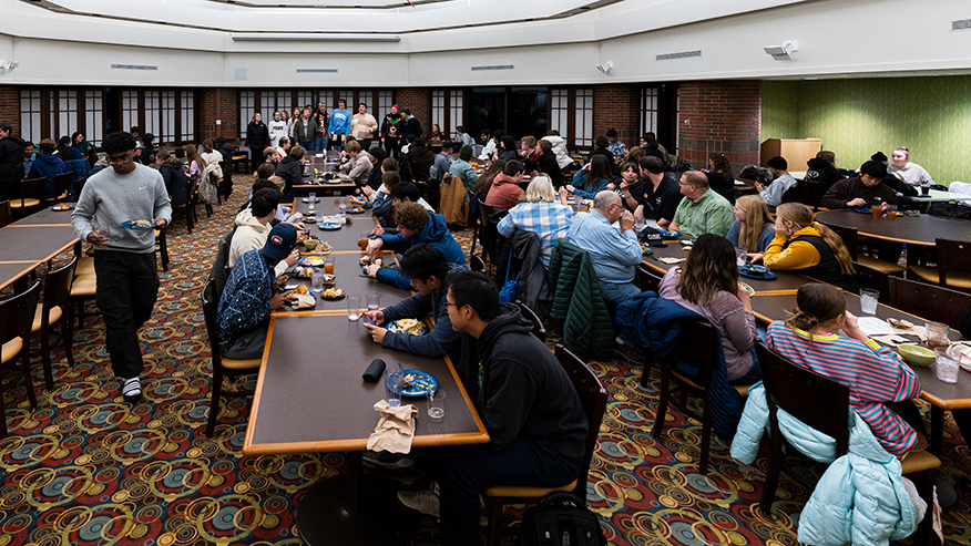 Students sit at tables eating Thanksgiving dinner