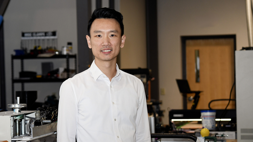 A Purdue researcher wearing a white dress shirt stands in an engineering laboratory and looks into the camera.