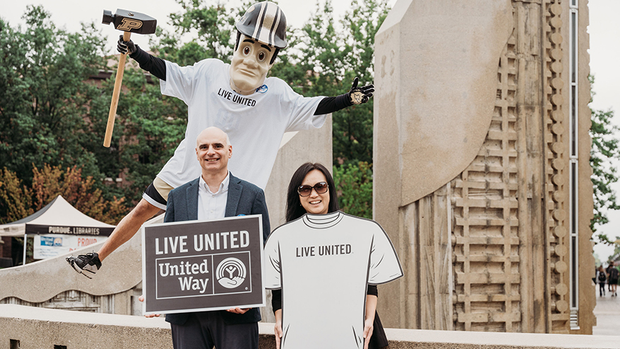 Two campaign leaders and Purdue Pete pose with United Way signage in front of the Engineering Fountain.