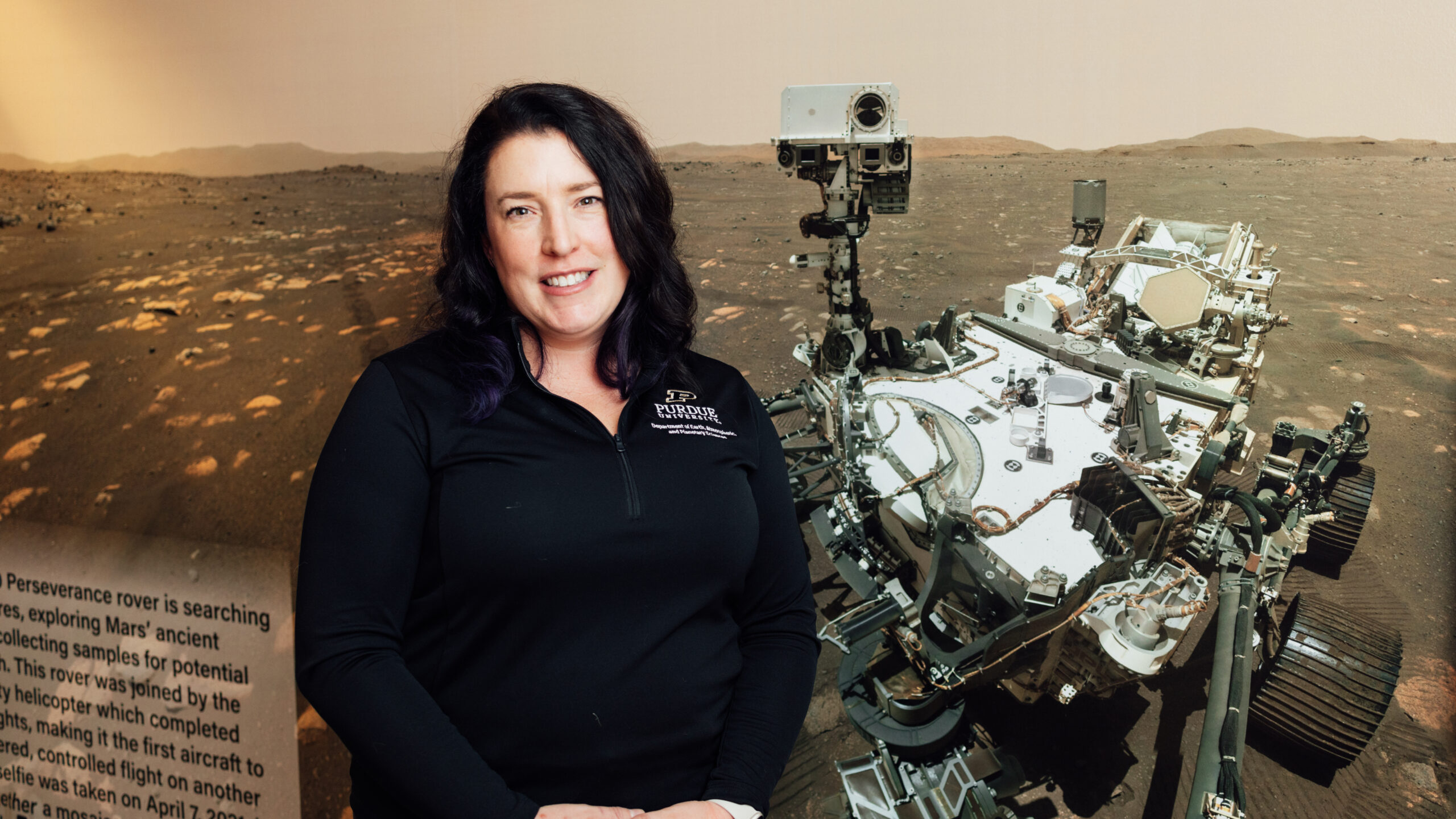 Purdue University professor Bryony Hogan stands in front of a photo of the Mars rover Perseverance.