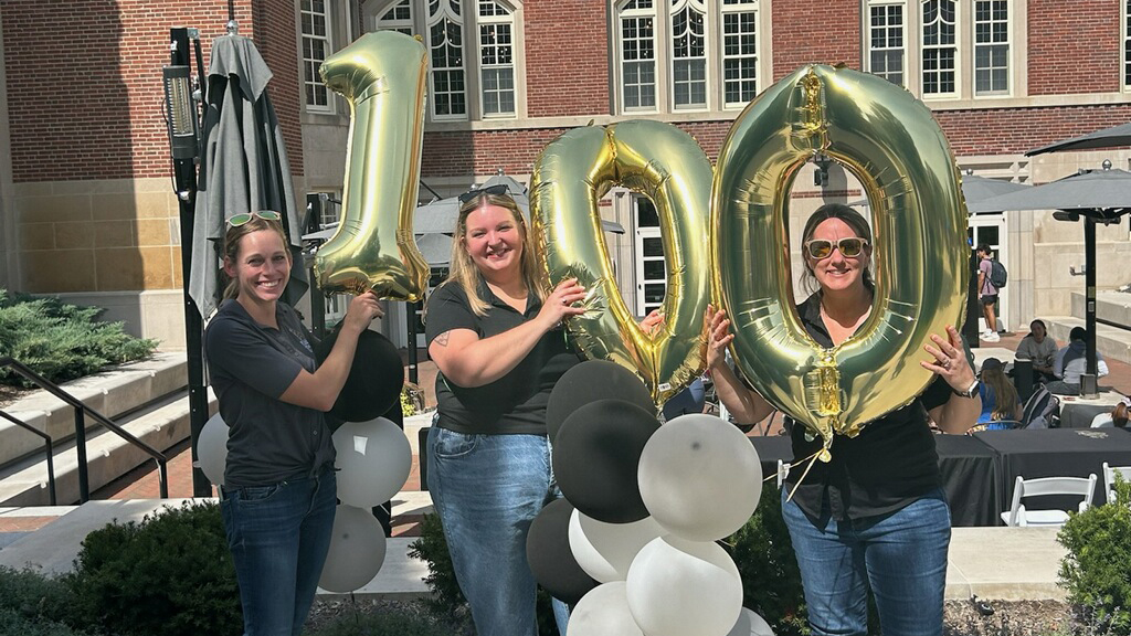 Three people stand in front of the Purdue Memorial Union with balloons.