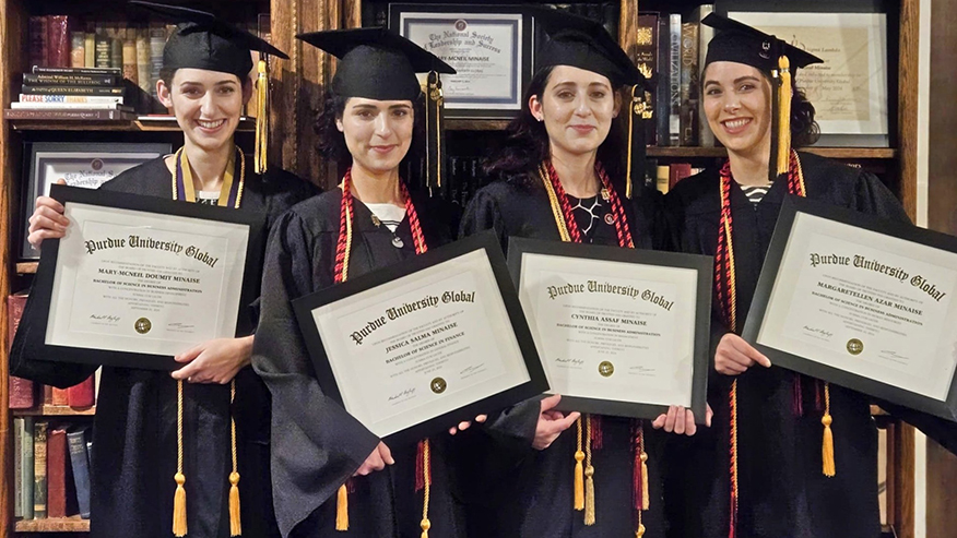 The Minaise sisters in graduation regalia smiling and holding their Purdue Global degrees