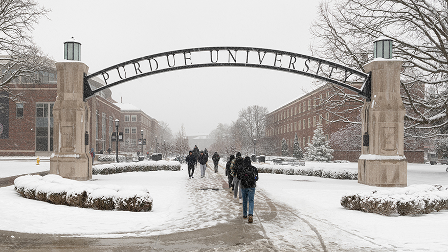 People walking under the Gateway to the Future arch on Purdue’s campus in snowy weather