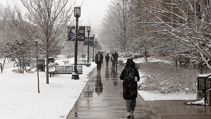 People walk on a Purdue University sidewalk in the snow on a cold winter day.