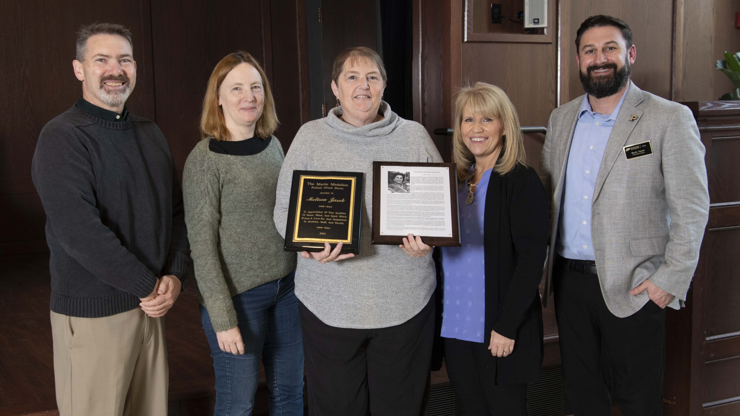 The award winner holds two plaques while standing alongside four Purdue employees at the award ceremony.