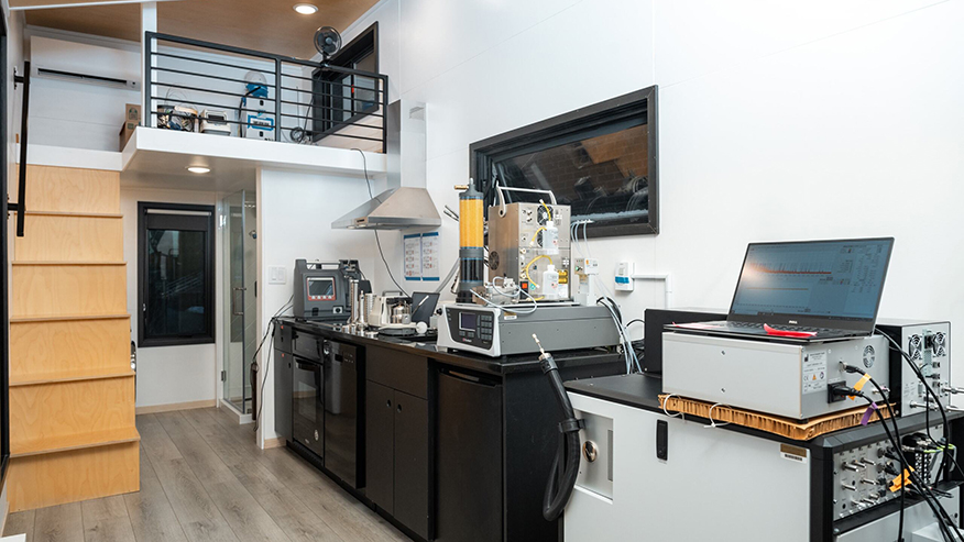 Various pieces measurement instrumentation surround a stove, sink and other appliances in a two-story house lab