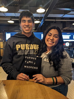 student and parent pose at event with sign for Purdue Family Weekend