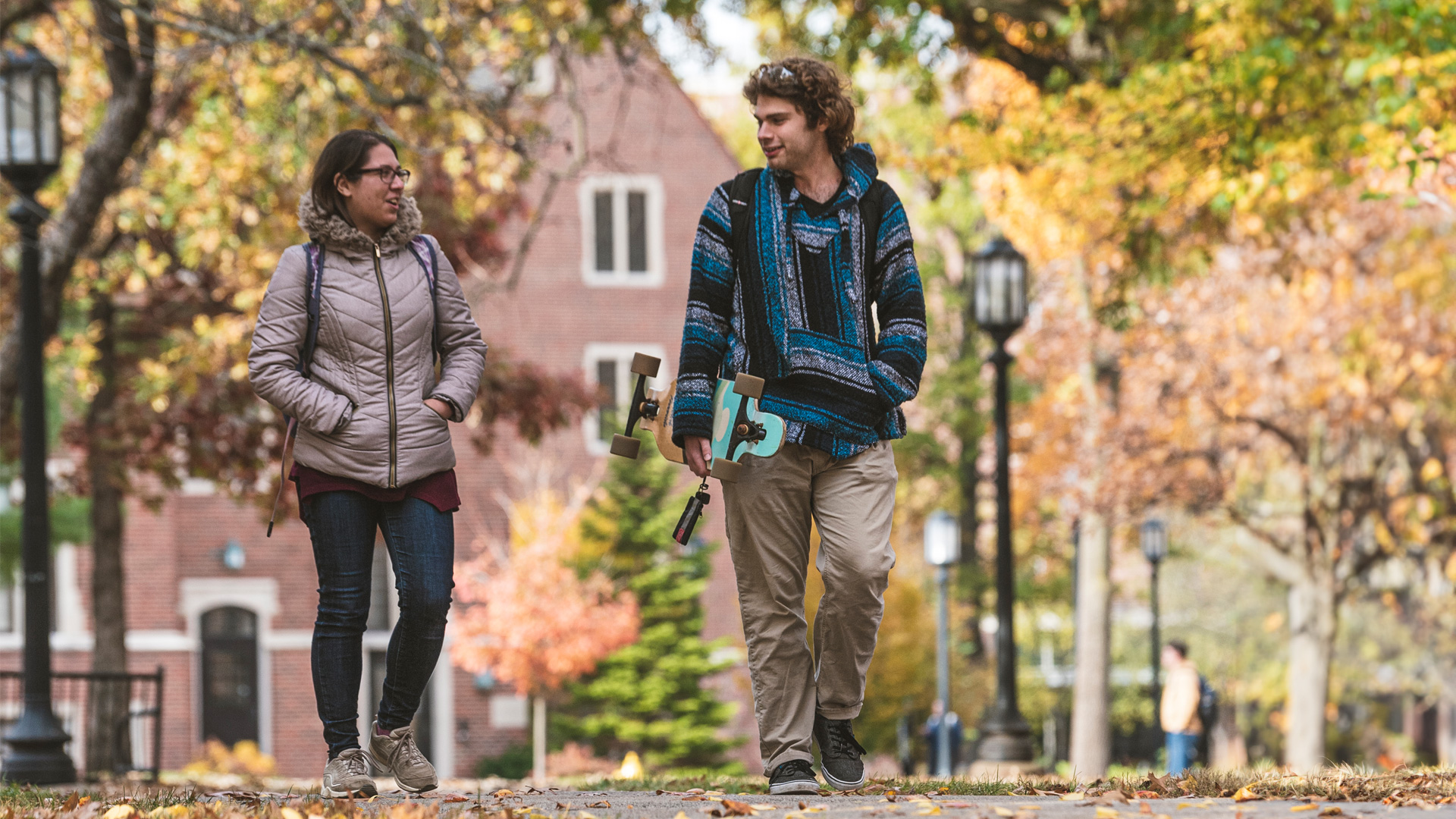 Two students walking on campus in the fall. 