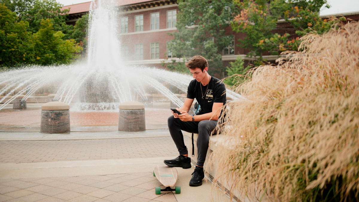 Student sitting near the Engineering fountain on the Purdue Mall. 