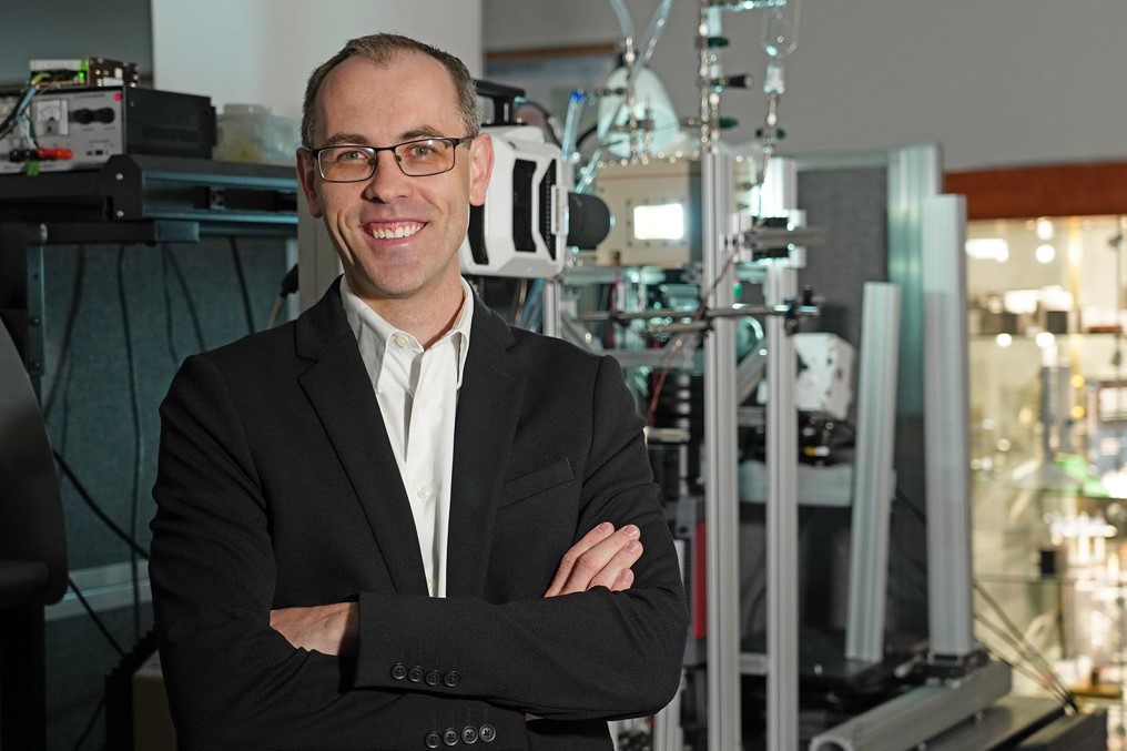 PI Justin A. Weibel standing in front of a laboratory facility for optical metrology of pool boiling.