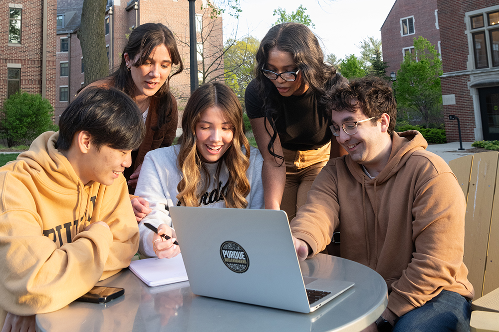 Students working outside around a laptop.