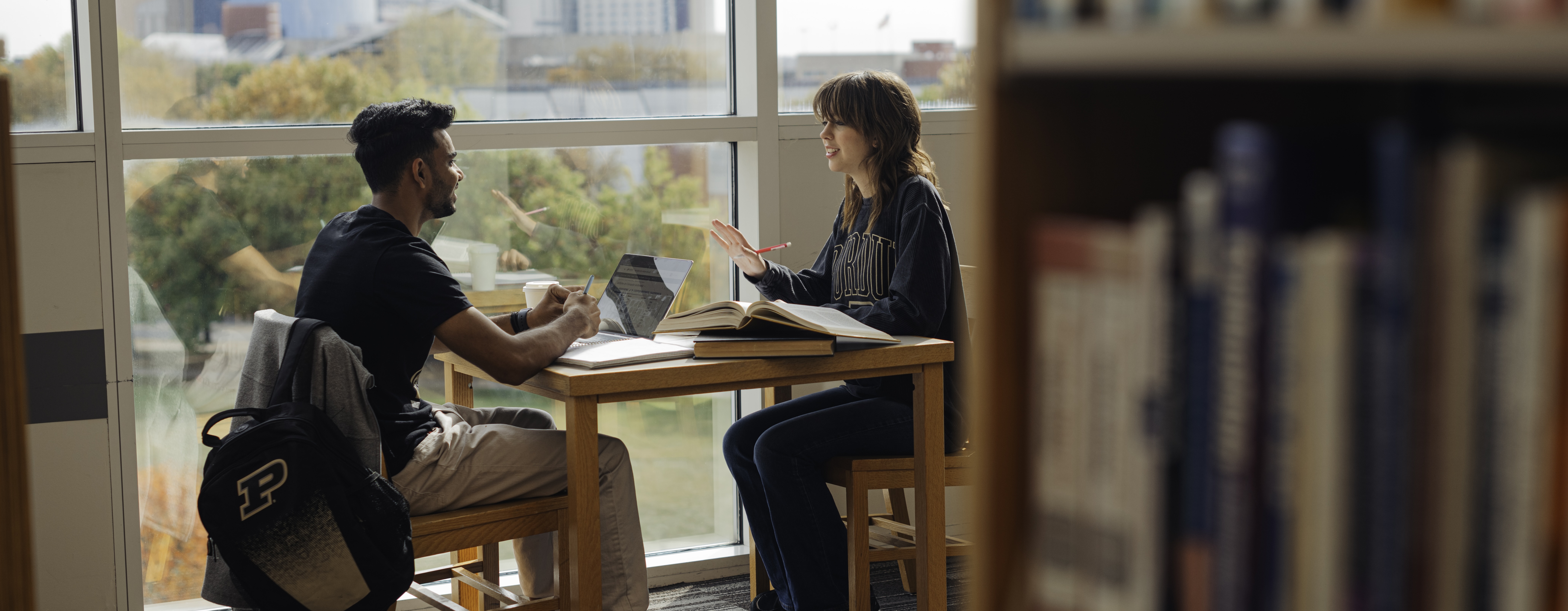 two Purdue students working together on laptops at a desk in a library