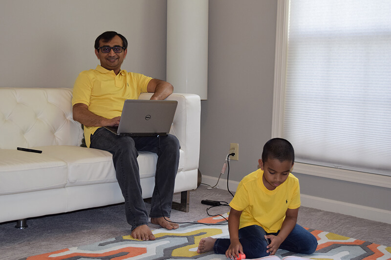 Mohammad Rahman sitting on couch and son playing with toys on floor