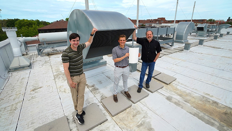 researchers on roof by air vent or intake