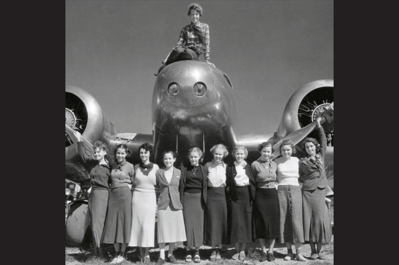 Amelia Earhart sitting on plane with students standing in front